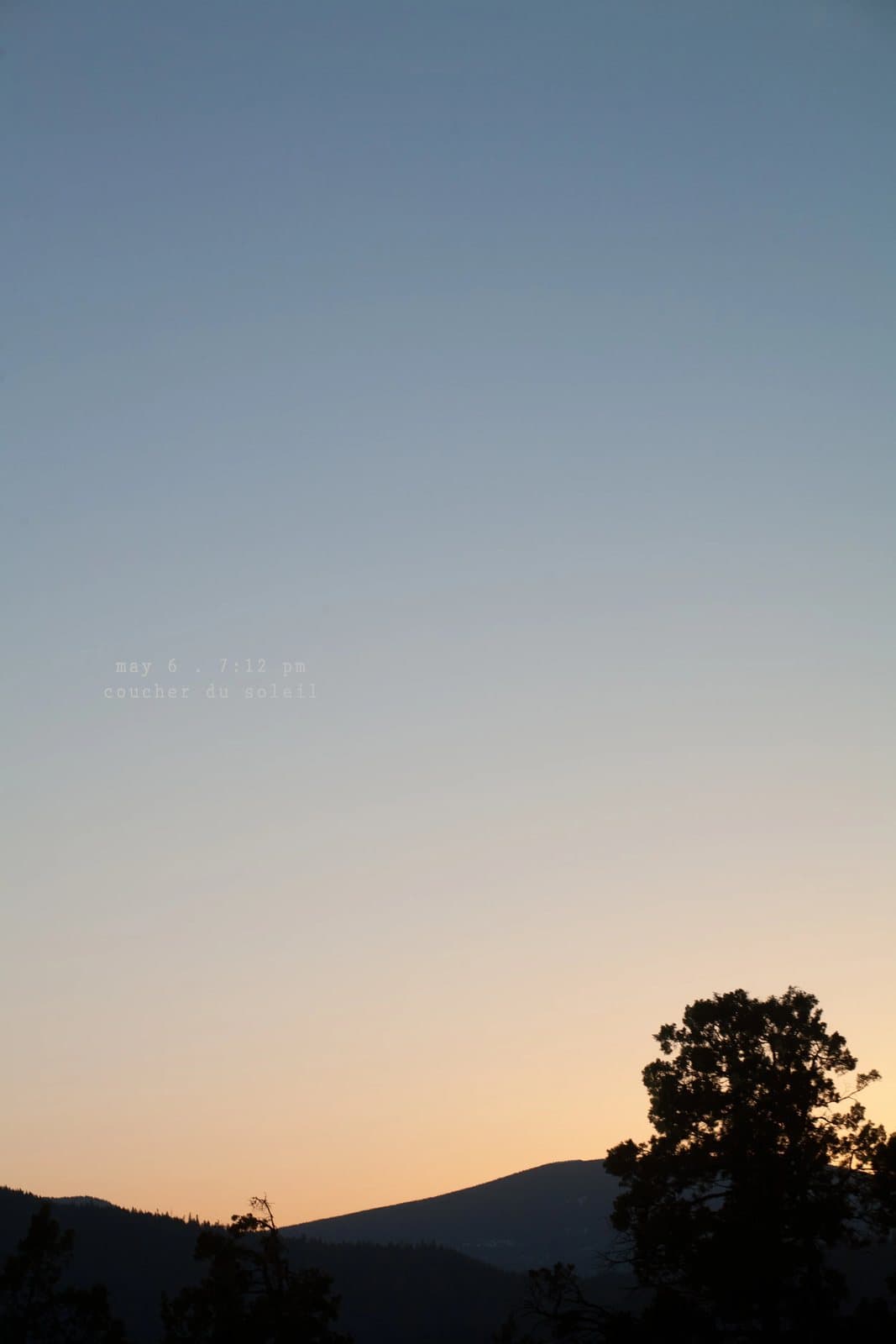 A clear sunset sky fades from blue to orange above silhouetted hills and trees.