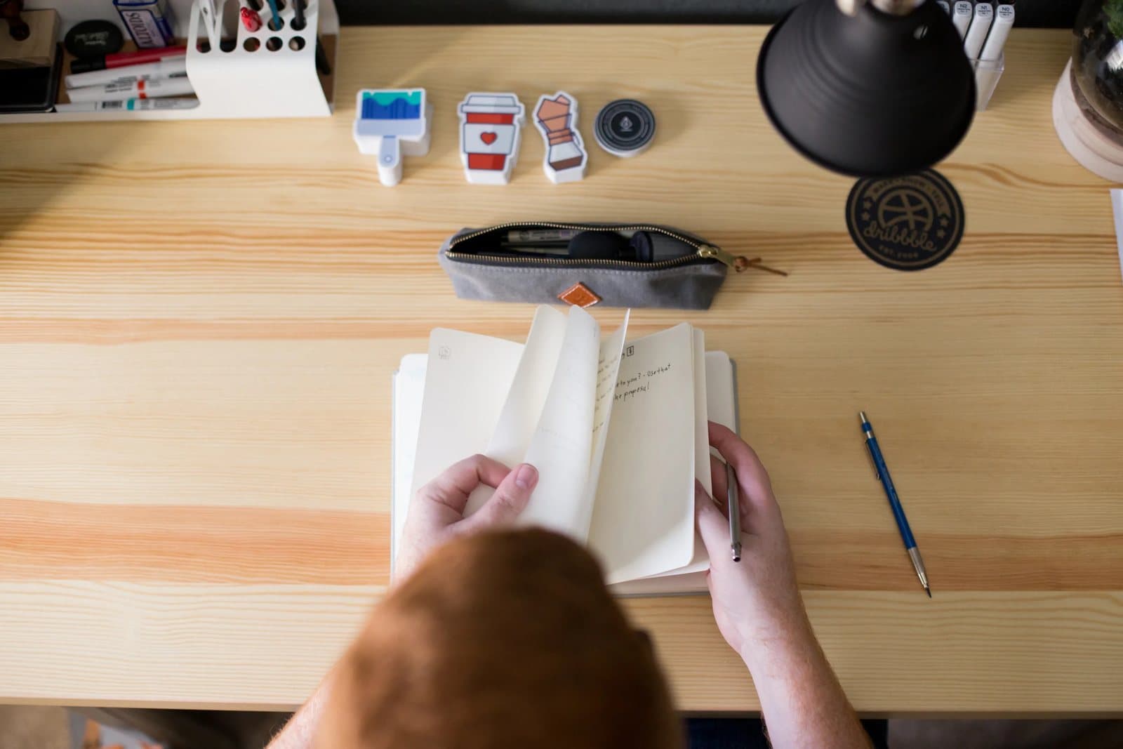From above, Kyle flips through a sketchbook on his desk among icon stickers and pens.