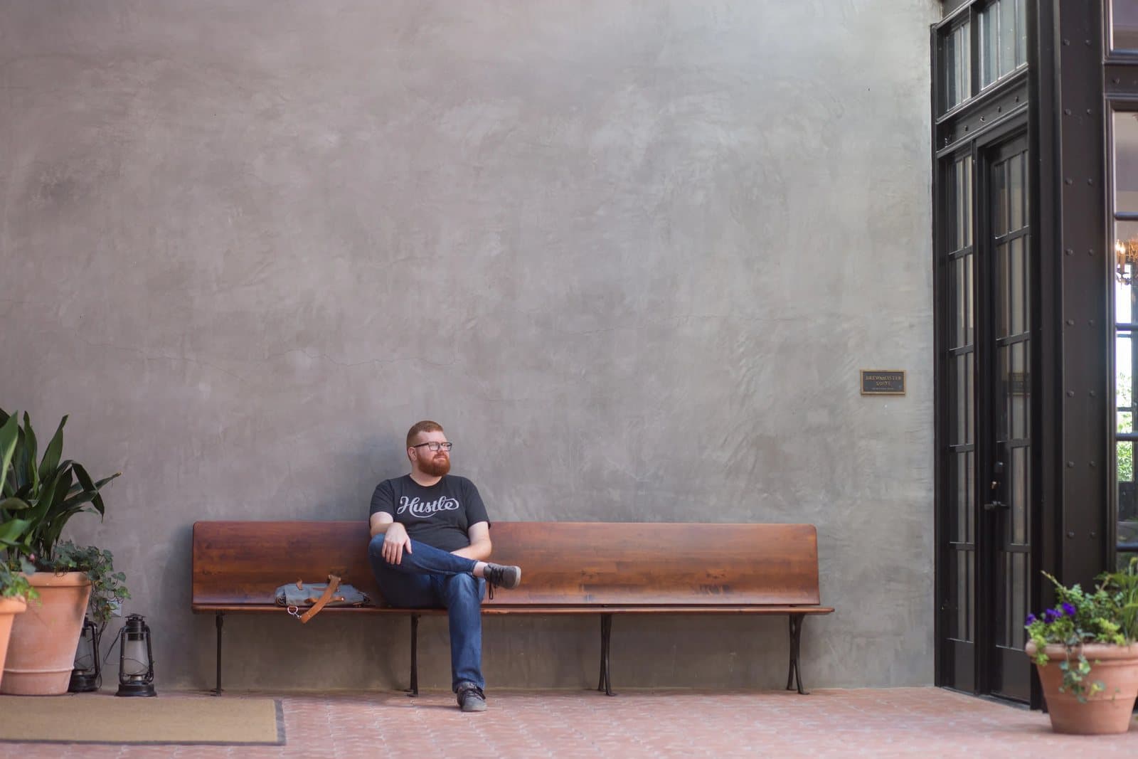 Kyle relaxes on a bench in a courtyard at the Pearl, beside tall black-framed doors.