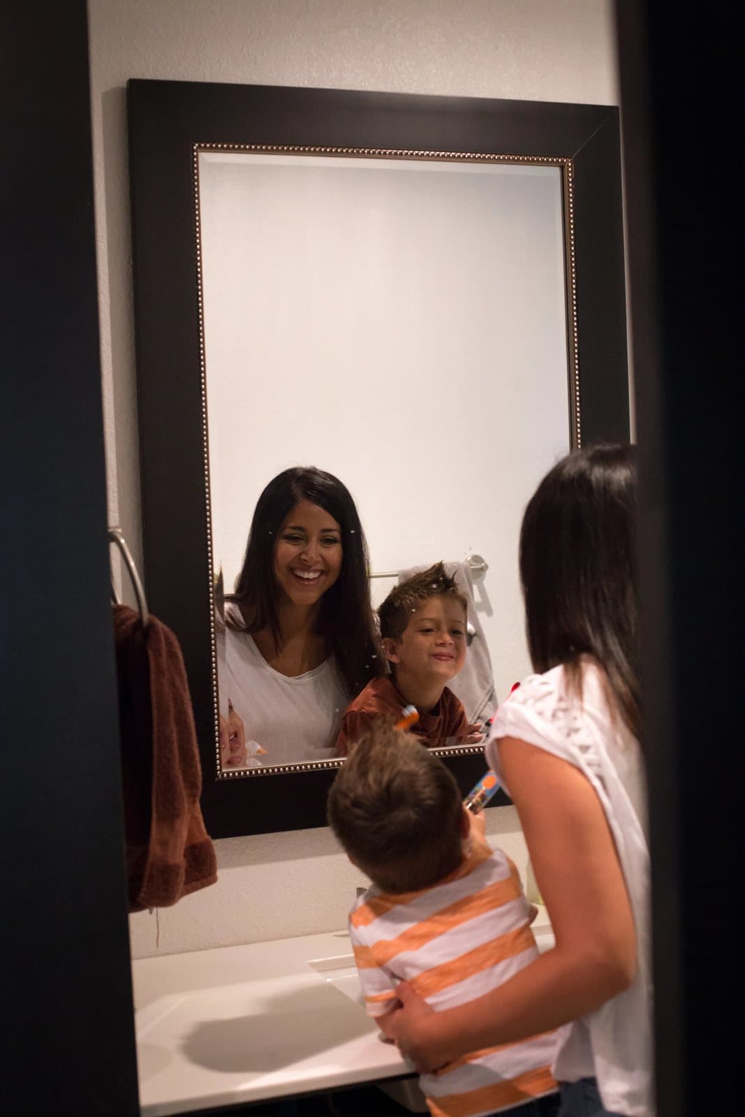Mom and the boys smile into the bathroom mirror while getting ready at the sink.