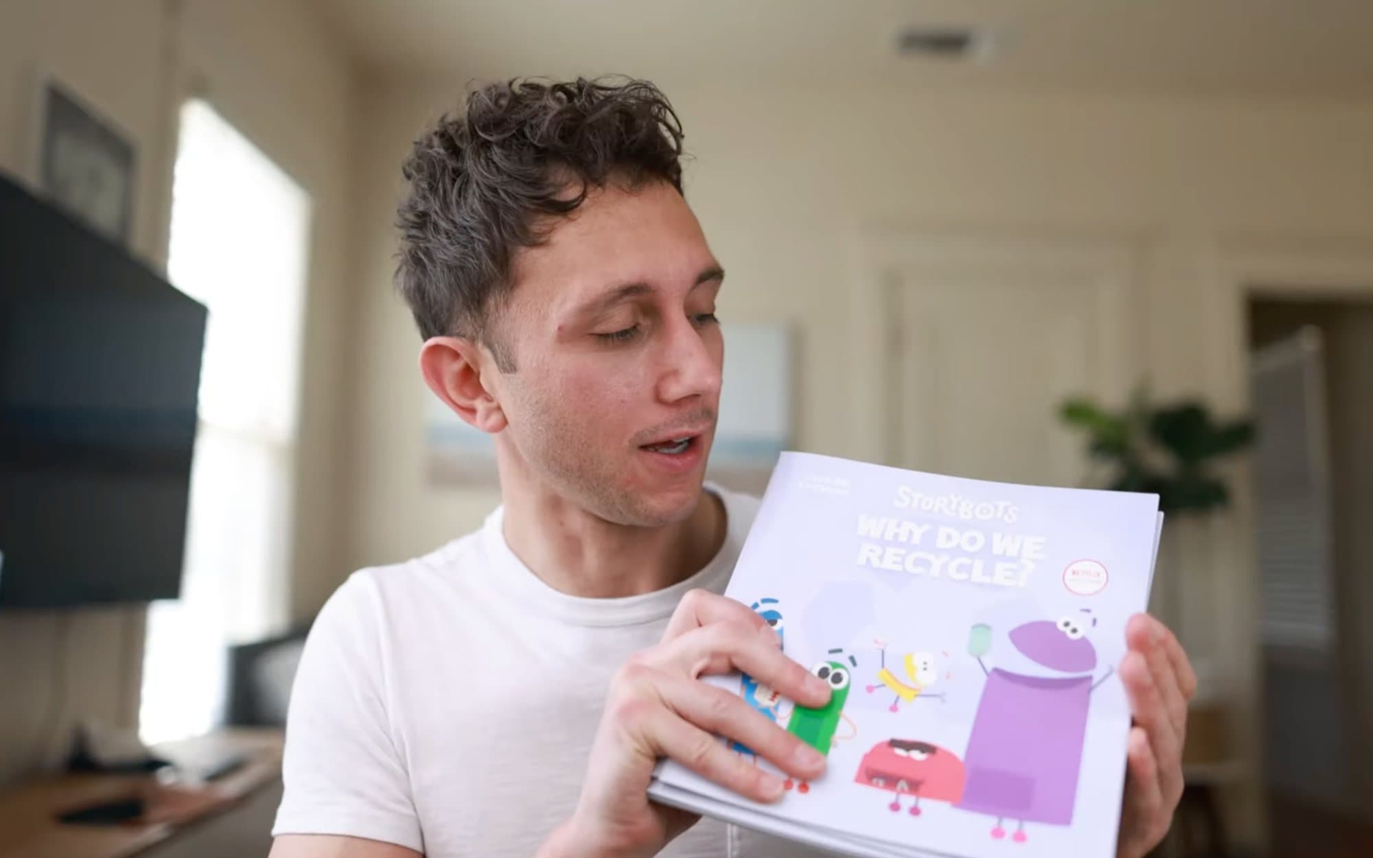 A man in a home office holds up Why Do We Recycle?, the StoryBots children's book collaboration.