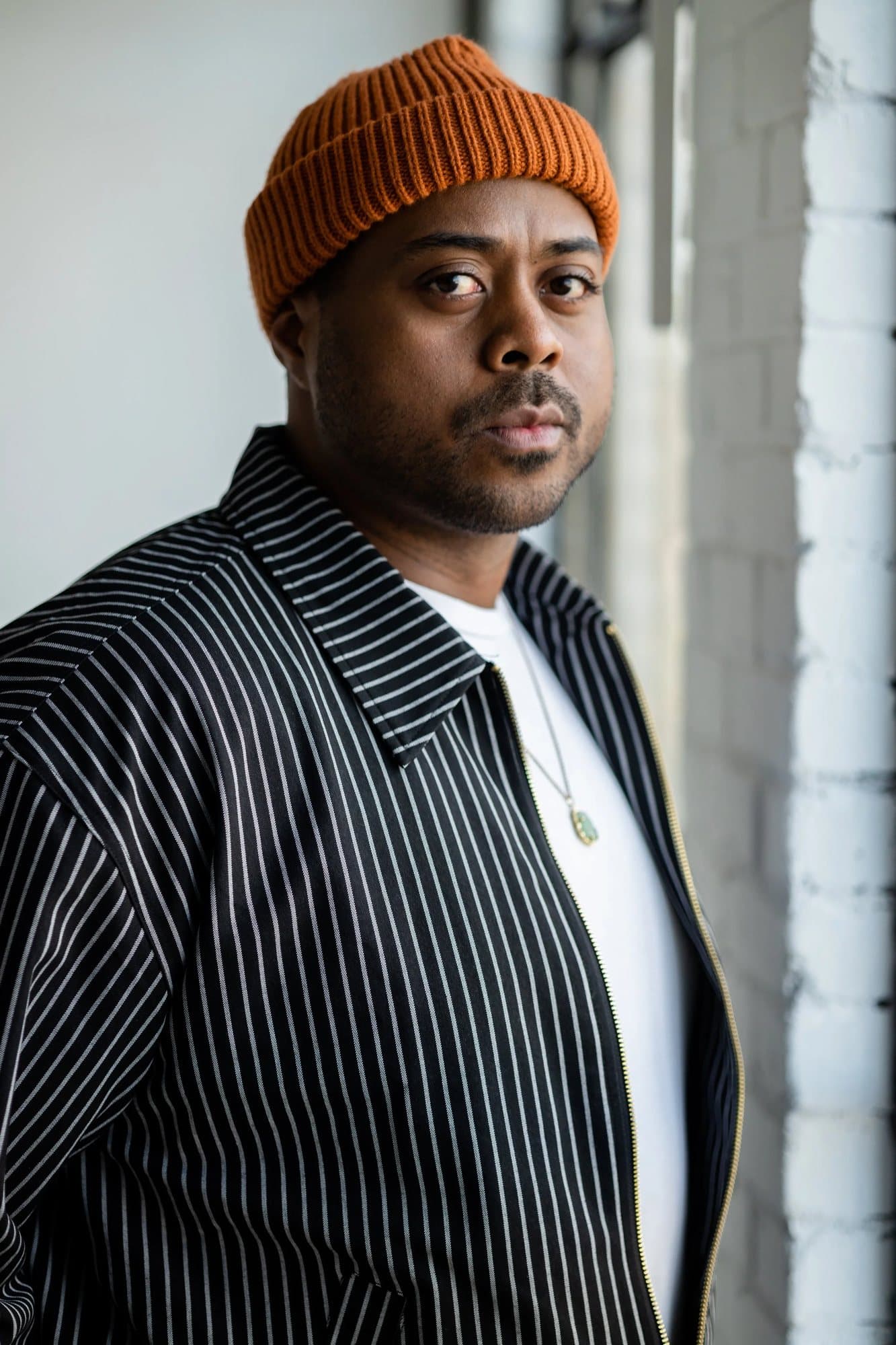 Roberto, featured in Volume 37, in an orange beanie and pinstriped jacket by a brick wall.